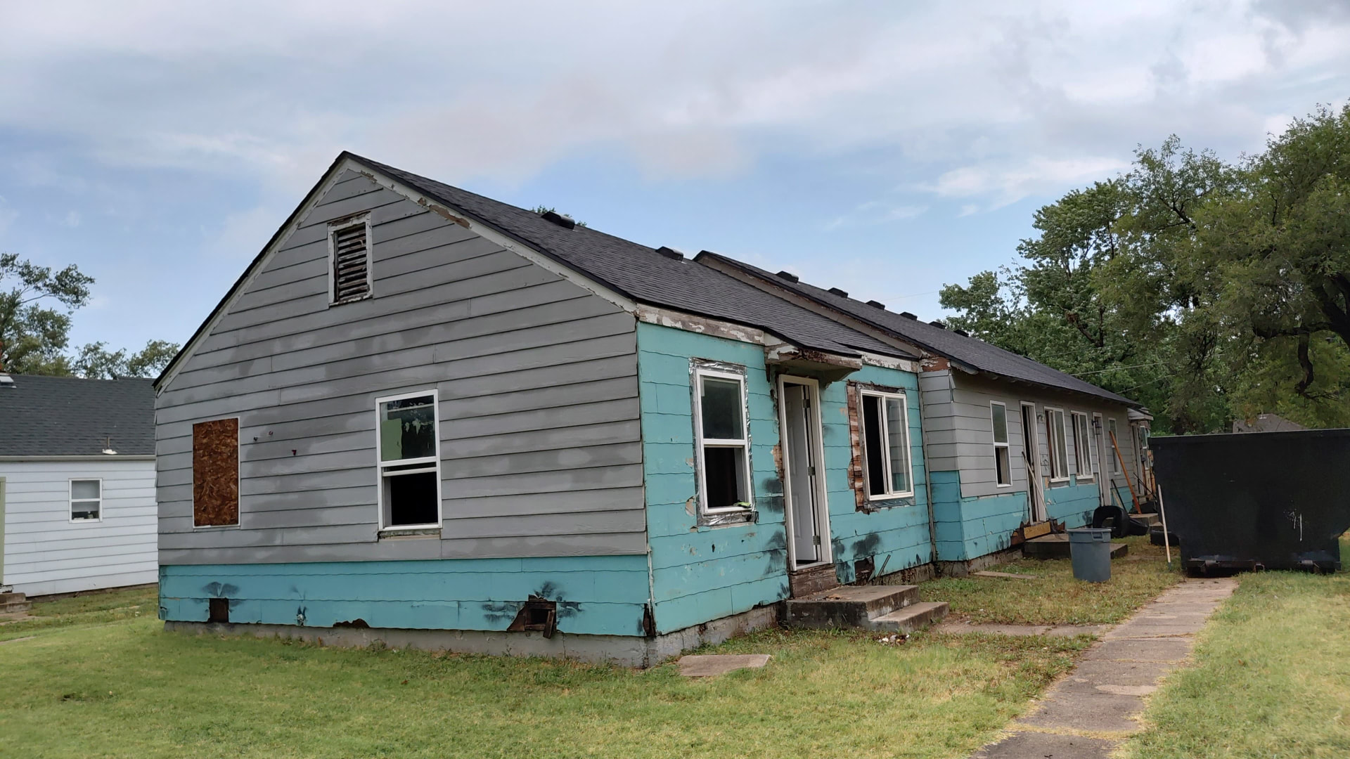 Wichita property before — failing painted siding and damaged trim