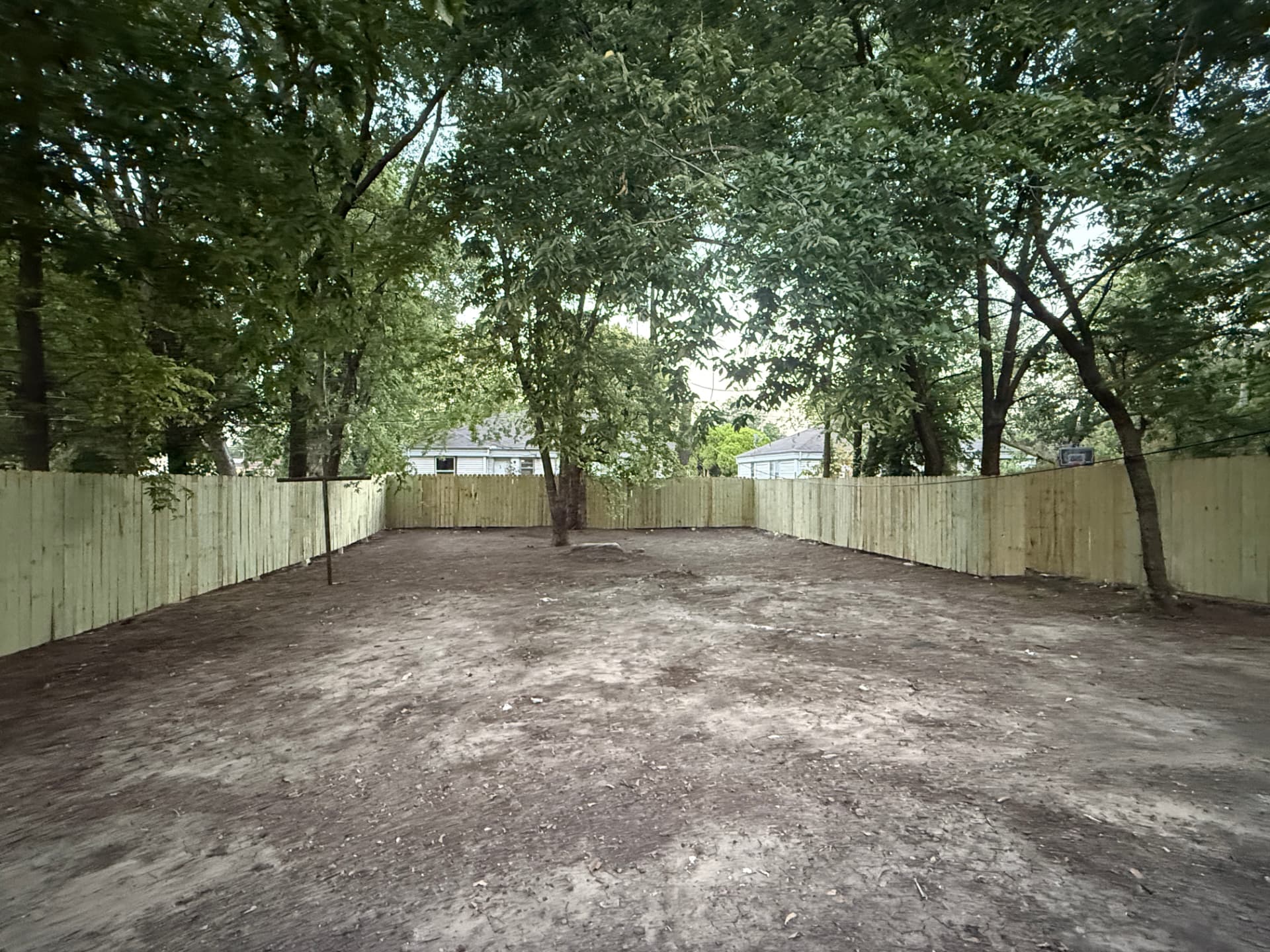 Cleared and graded backyard behind a new privacy fence, debris and overgrowth removed