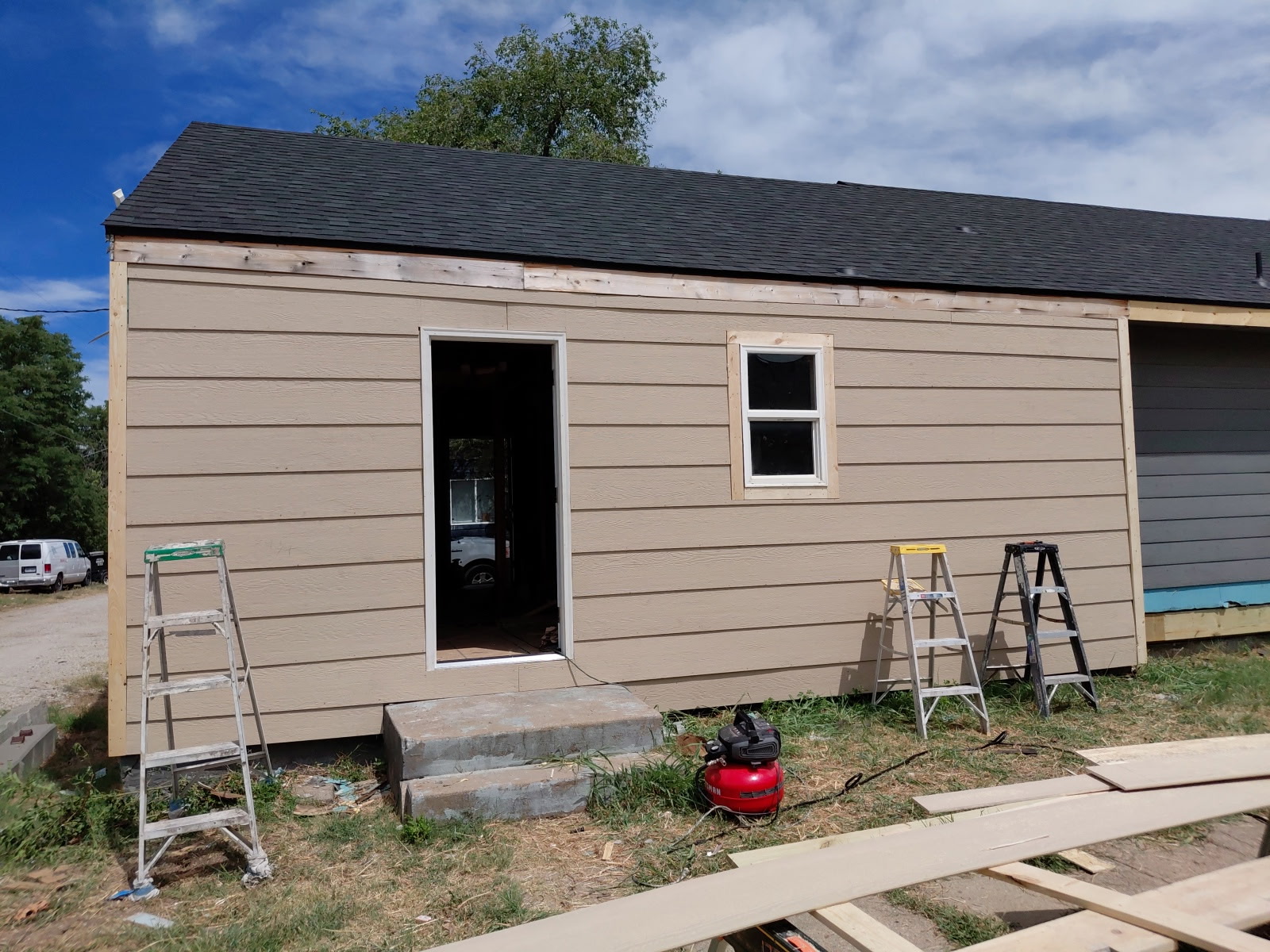 New lap siding installed over fresh framing with ladders and compressor on site, siding and prep underway