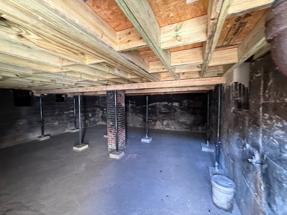Rebuilt floor framing over a cleared crawlspace, temporary jack posts carrying the new beam
